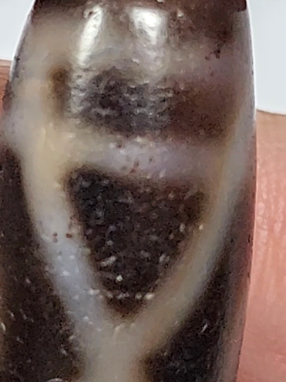 Antique two-eye dzi bead close-up, dark agate with cream white eye motifs, visible bloodspots and aged surface patina