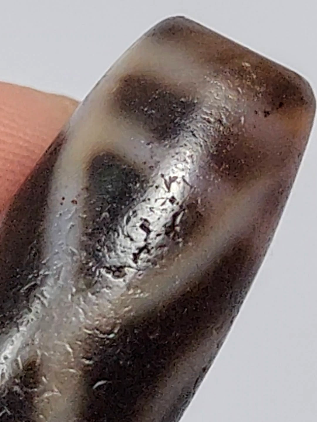 Antique two-eye dzi bead agate dark brown white eye motif bloodspots aged patina surface close-up held by fingers