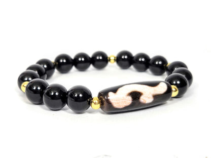Full bracelet view: vintage Ruyi dzi focal bead centred on a strand of polished black agate rounds with gold-plated accent beads, photographed on white — Ancient Dzi Shop