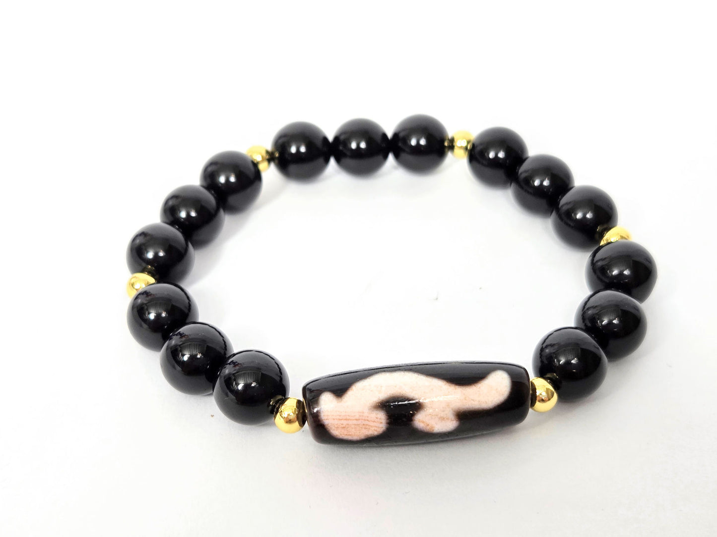 Overhead lifestyle shot of complete black agate and Ruyi dzi bracelet laid flat, unretouched — bloodspot detail visible on the focal bead, Ancient Dzi Shop