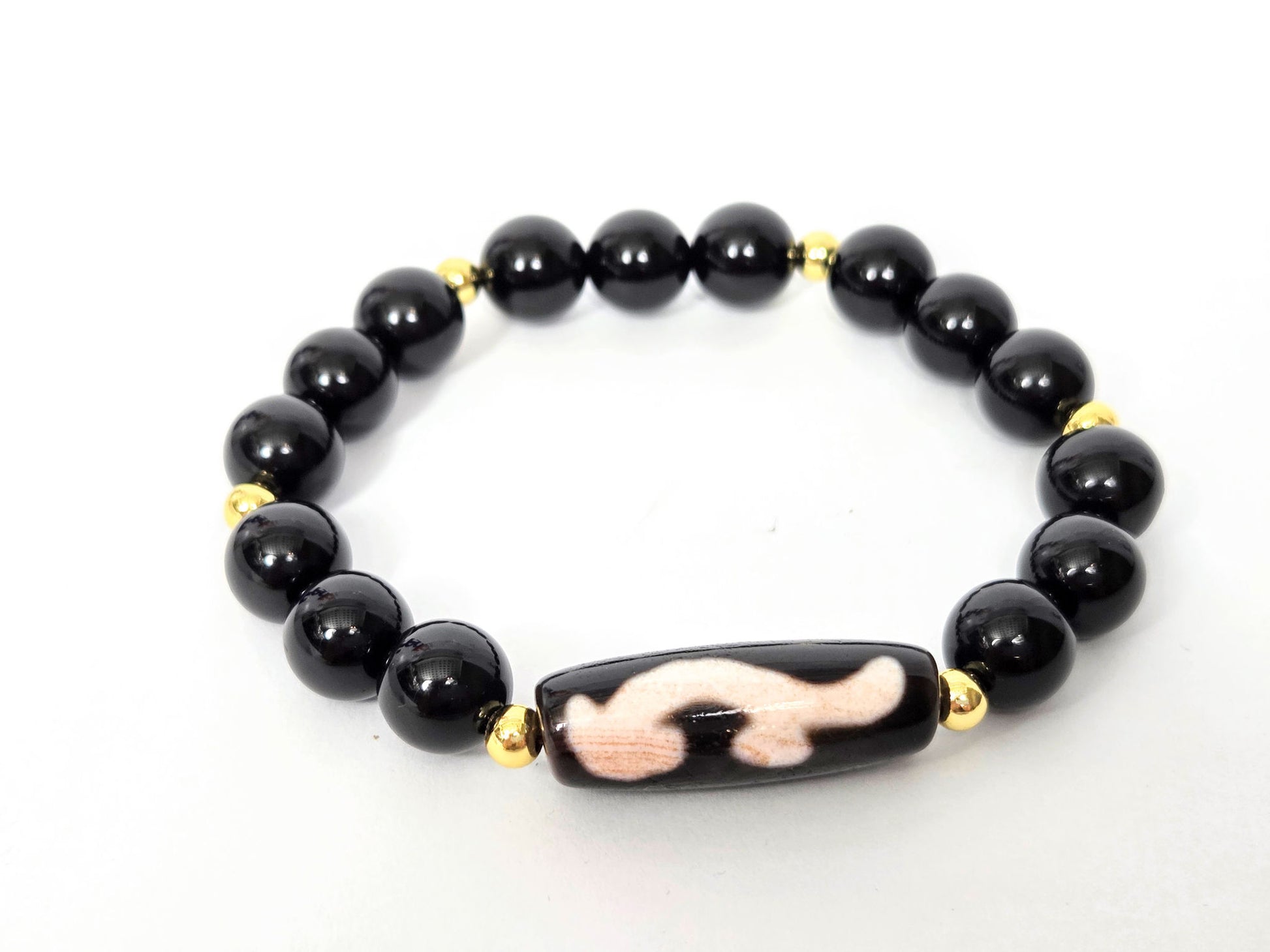 Overhead lifestyle shot of complete black agate and Ruyi dzi bracelet laid flat, unretouched — bloodspot detail visible on the focal bead, Ancient Dzi Shop