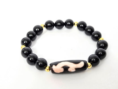 Overhead lifestyle shot of complete black agate and Ruyi dzi bracelet laid flat, unretouched — bloodspot detail visible on the focal bead, Ancient Dzi Shop