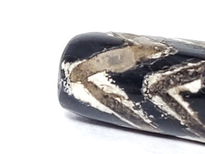 Extreme macro of bead end on ancient Four-Row Tiger Tooth Dzi — raised calcification mounds contrast with smooth black agate tip, tiger tooth etching visible beneath mineral deposits