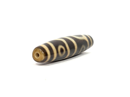 Opposite angled end view of new four eye variant dzi bead N-102526-4EVS showing the second drill hole in a translucent honey-amber tip, cream end bands and a framed eye close to that end, dark brown agate body