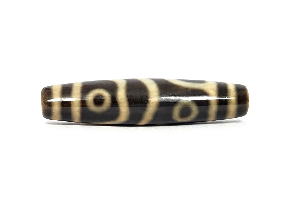 New four eye variant dzi bead N-102526-4EVS, first face — cream-white eye centered between a forked Y-shaped line and a diagonal divider, second eye visible at the upper edge, high-gloss dark brown to black agate, cream bands at both ends