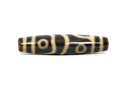 New four eye variant dzi bead N-102526-4EVS, first face — cream-white eye centered between a forked Y-shaped line and a diagonal divider, second eye visible at the upper edge, high-gloss dark brown to black agate, cream bands at both ends