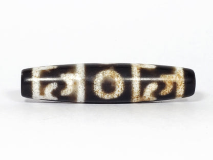 N-062226-GRRP, Guru Rinpoche ritual paraphernalia dzi, 57.6×13.5mm, very dark brown, face A, sandy-cream motif, unretouched