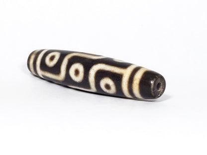 N-062226-9E2, angled view toward narrow tapered tip, drill hole centred, nine eye motif wrapping body, unretouched