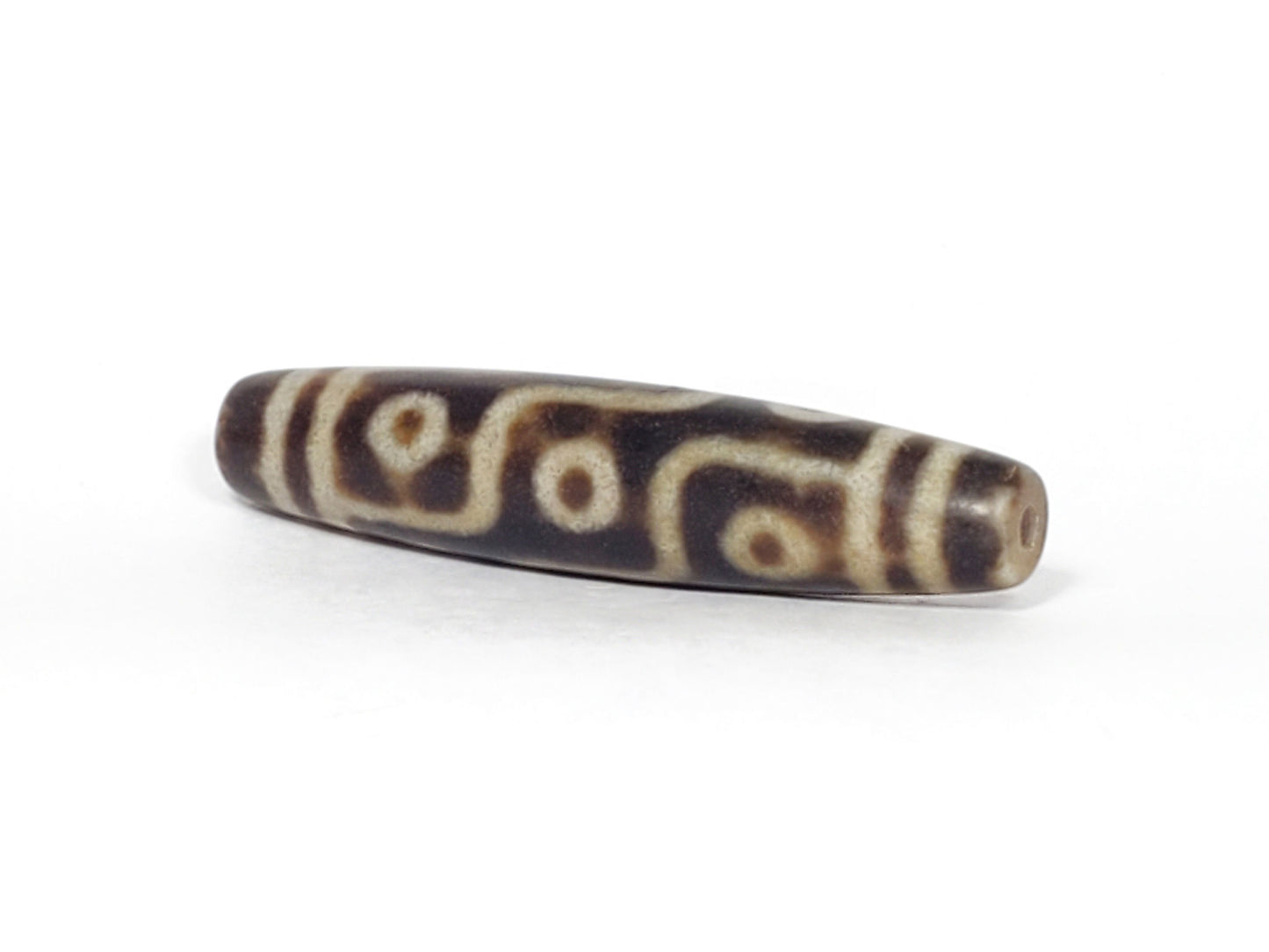 N-062226-9E3, angled view toward one tapered end, drill hole centred, nine eye motif wrapping body, unretouched