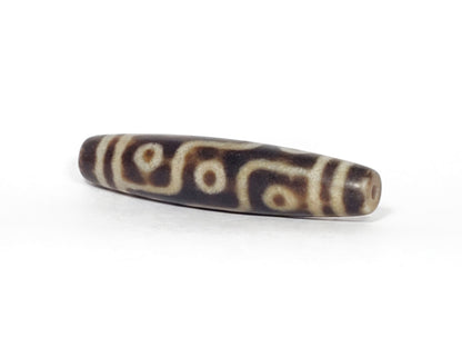 N-062226-9E3, angled view toward one tapered end, drill hole centred, nine eye motif wrapping body, unretouched