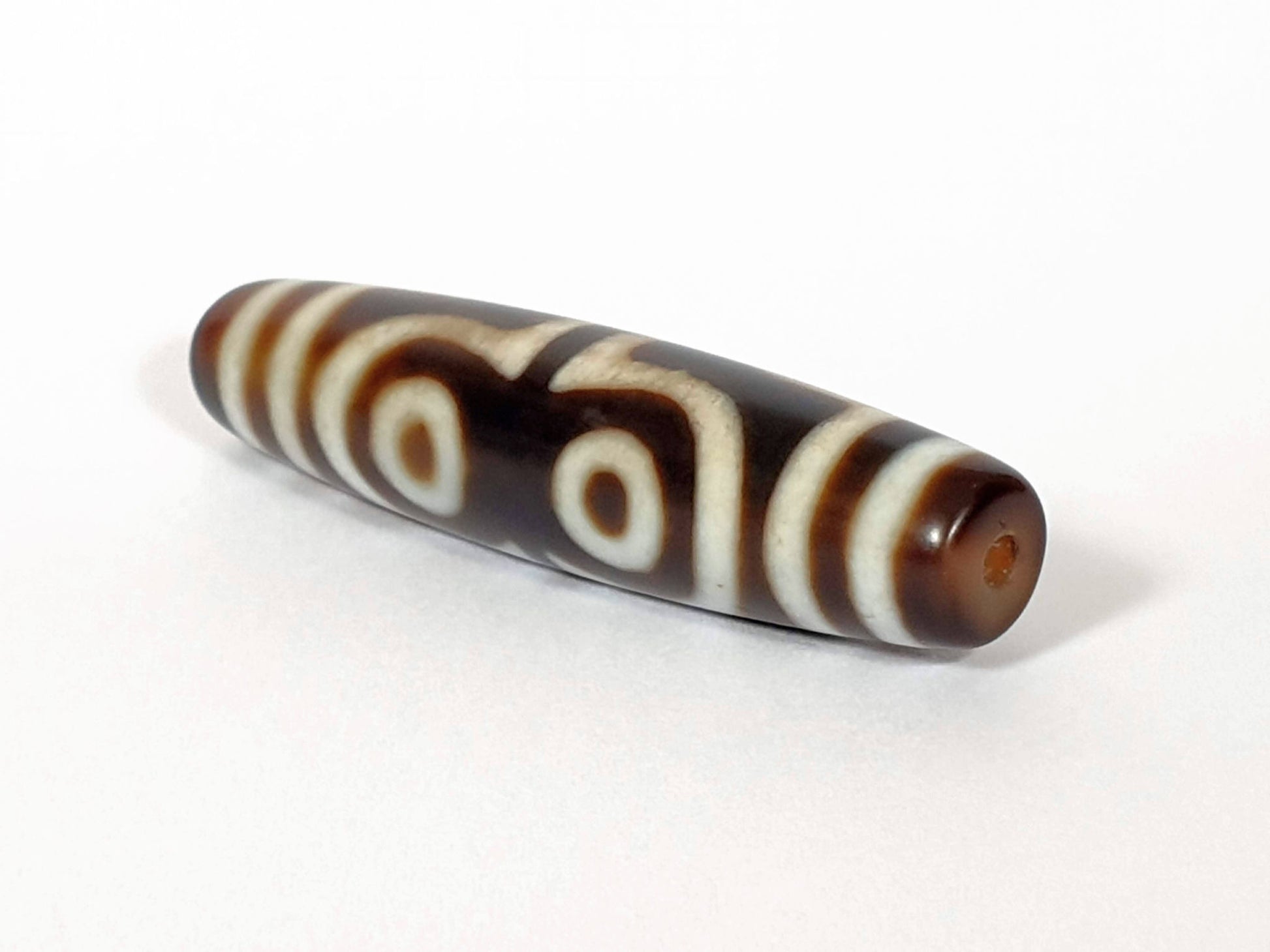 N-062426-4E new four eye dzi 58.5x13.9mm angled view asymmetric taper drill hole end warm brown agate unretouched