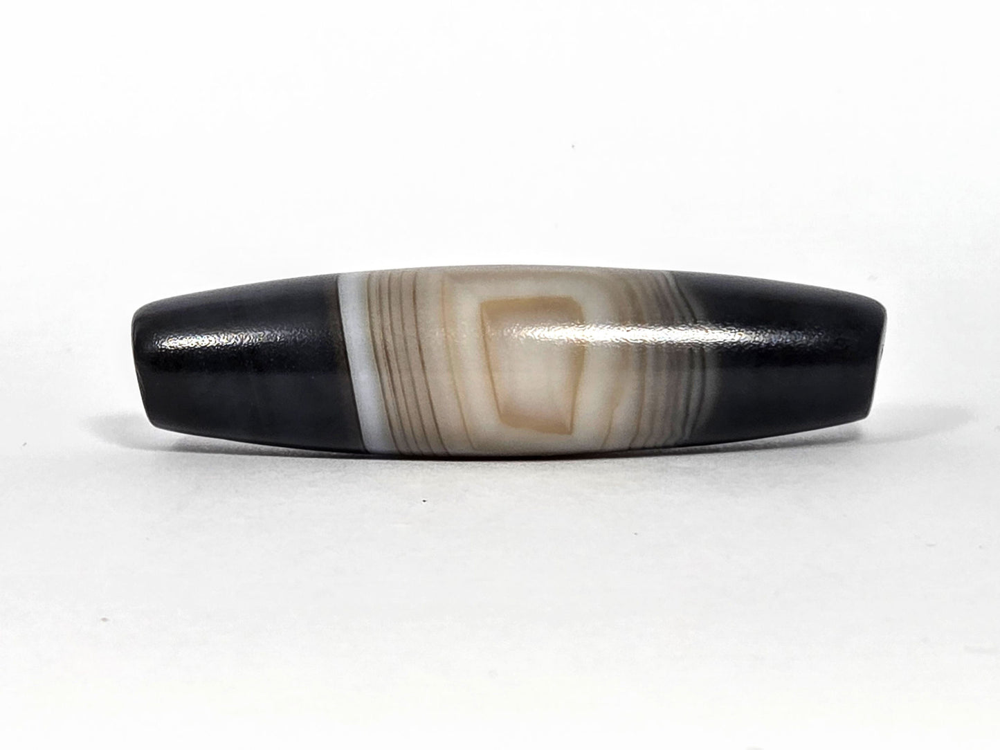 N-N-080426-1E5 natural one eye dzi bead 54.4×14.1mm, Face A showing resolved concentric oval eye in warm beige banding against pitch-black ends, unretouched