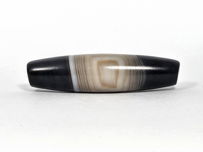 N-N-080426-1E5 natural one eye dzi bead 54.4×14.1mm, Face A showing resolved concentric oval eye in warm beige banding against pitch-black ends, unretouched