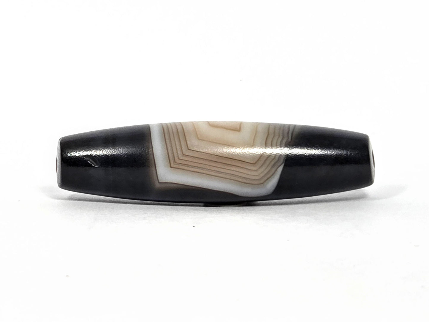 N-N-080426-1E5 natural one eye dzi bead 54.4×14.1mm, Face B showing parallel banding lines and stepped concentric pattern from this angle, unretouched