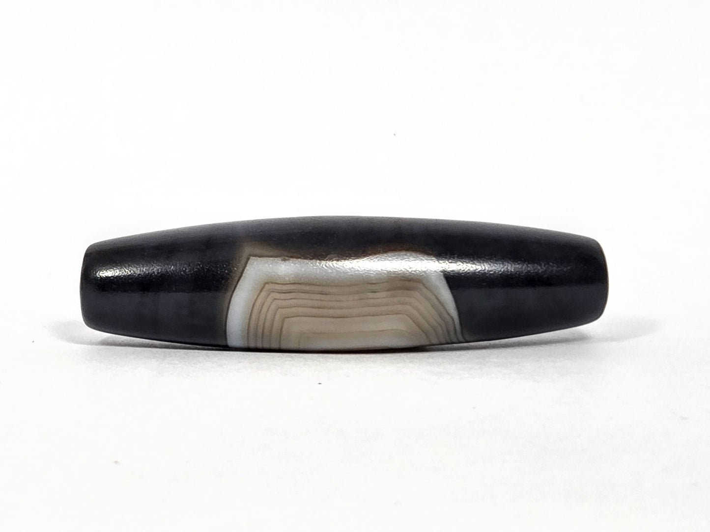 N-N-080426-1E5 natural one eye dzi bead 54.4×14.1mm, opposite turn showing broad cream-grey banding arc and concentric lines, no distinct eye, unretouched