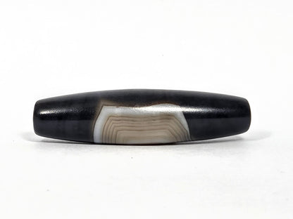 N-N-080426-1E5 natural one eye dzi bead 54.4×14.1mm, opposite turn showing broad cream-grey banding arc and concentric lines, no distinct eye, unretouched