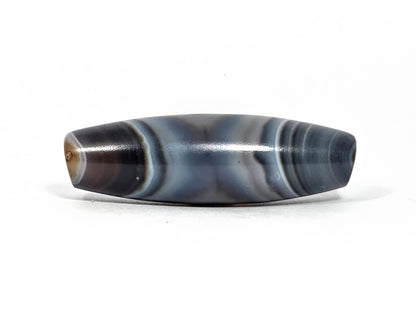 N-N-080926-1E6 natural one eye dzi bead 50.5×15.8mm, turn view showing warm dark brown drill end zone and parallel blue-grey body banding, unretouched