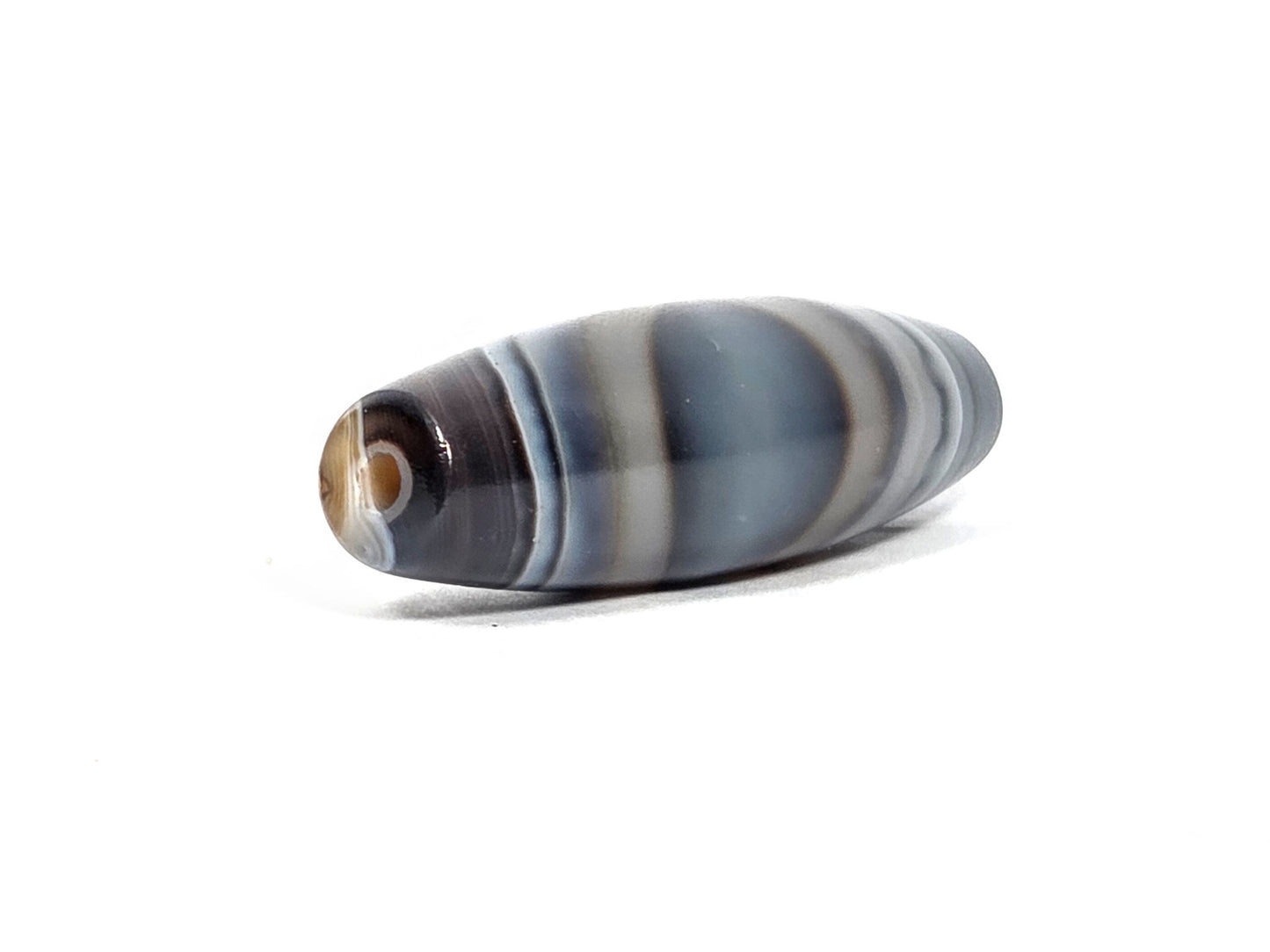 N-N-080926-1E6 natural one eye dzi bead 50.5×15.8mm, angled drill-end view showing dark end cap, cream shoulder stripe, and blue-grey body, unretouched