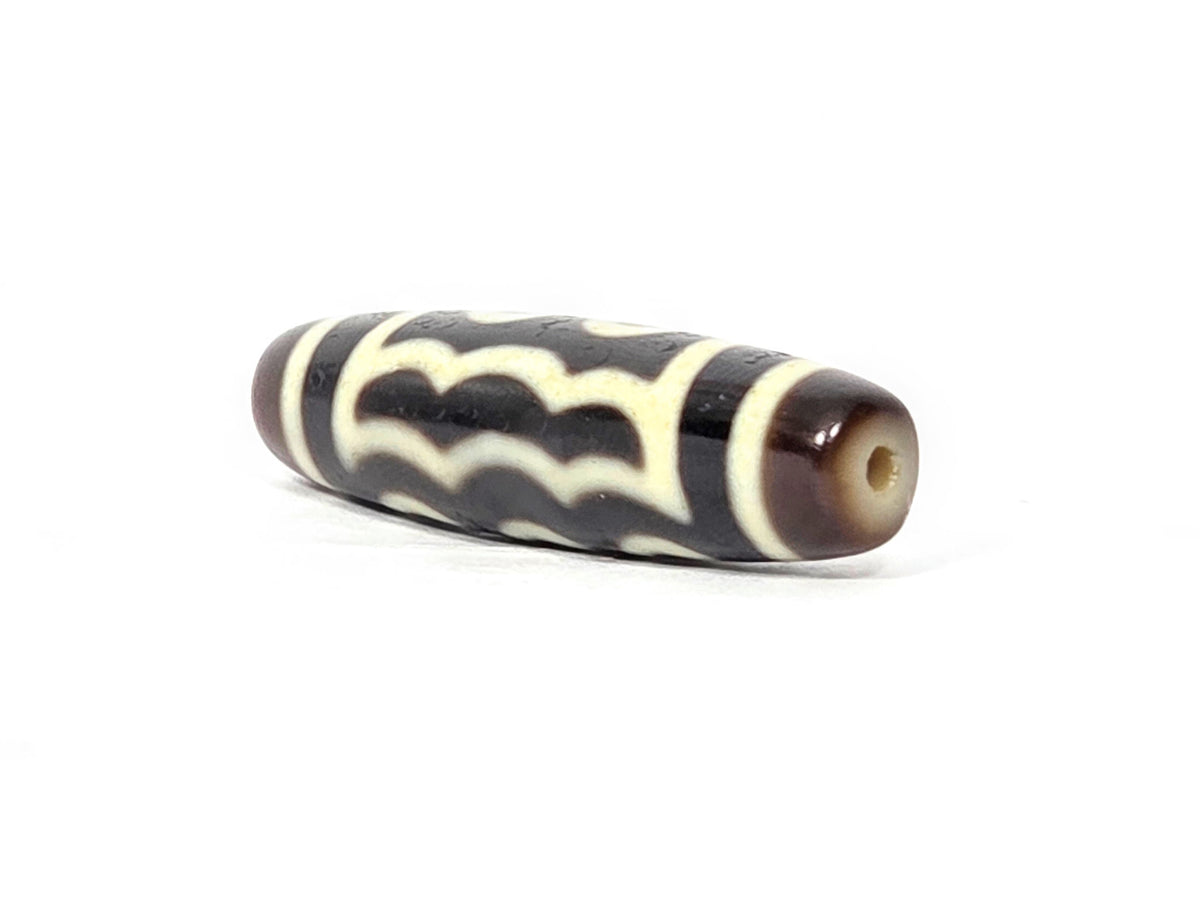 Five-eye dzi bead, dark brown agate, white wave motifs, visible drill hole, aged patina, 41mm barrel shape