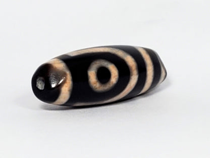 N-062426-2E new two eye dzi 37.7x13.0mm angled view opposite end pitch-black tip drill hole warm peach motif unretouched
