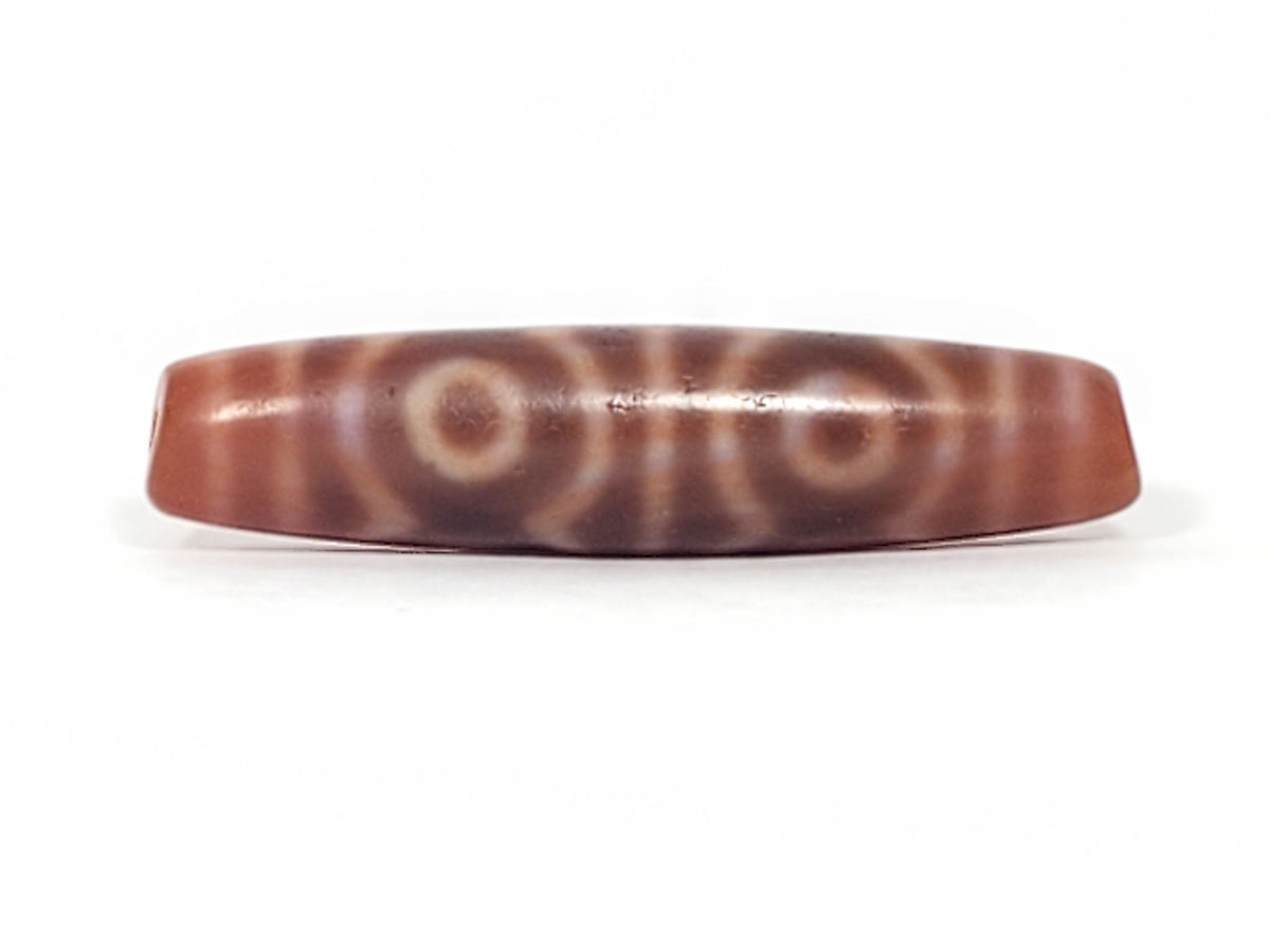 At-082624-6EBS, angled end-cap view, warm terracotta-rose cap, vivid orange-red drilled hole, six eye motif, unretouched