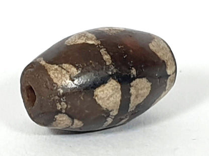 Antique double wave dzi — opposite angled end, drill hole at dark left tip, weathered cream wave zones on body, At-0426-DW2