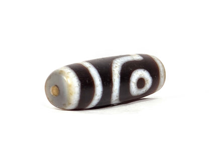 V-062126-2E dzi bead, angled view showing pale grey-white end cap and drill hole, unretouched