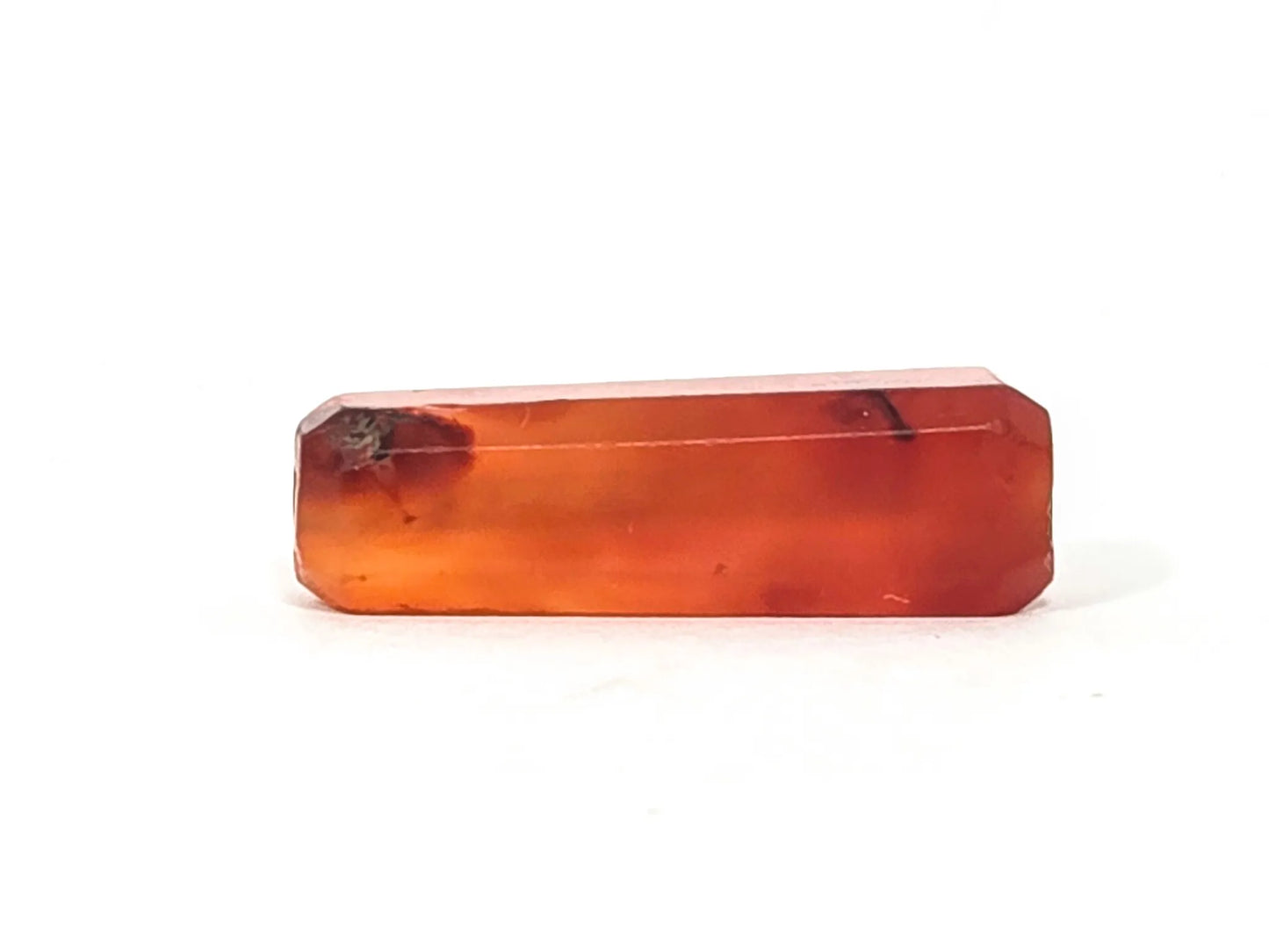 Second face of ancient beveled rectangular carnelian bead — translucent orange-red natural stone with dark natural inclusion, beveled edges visible, 500–1,000 years old
