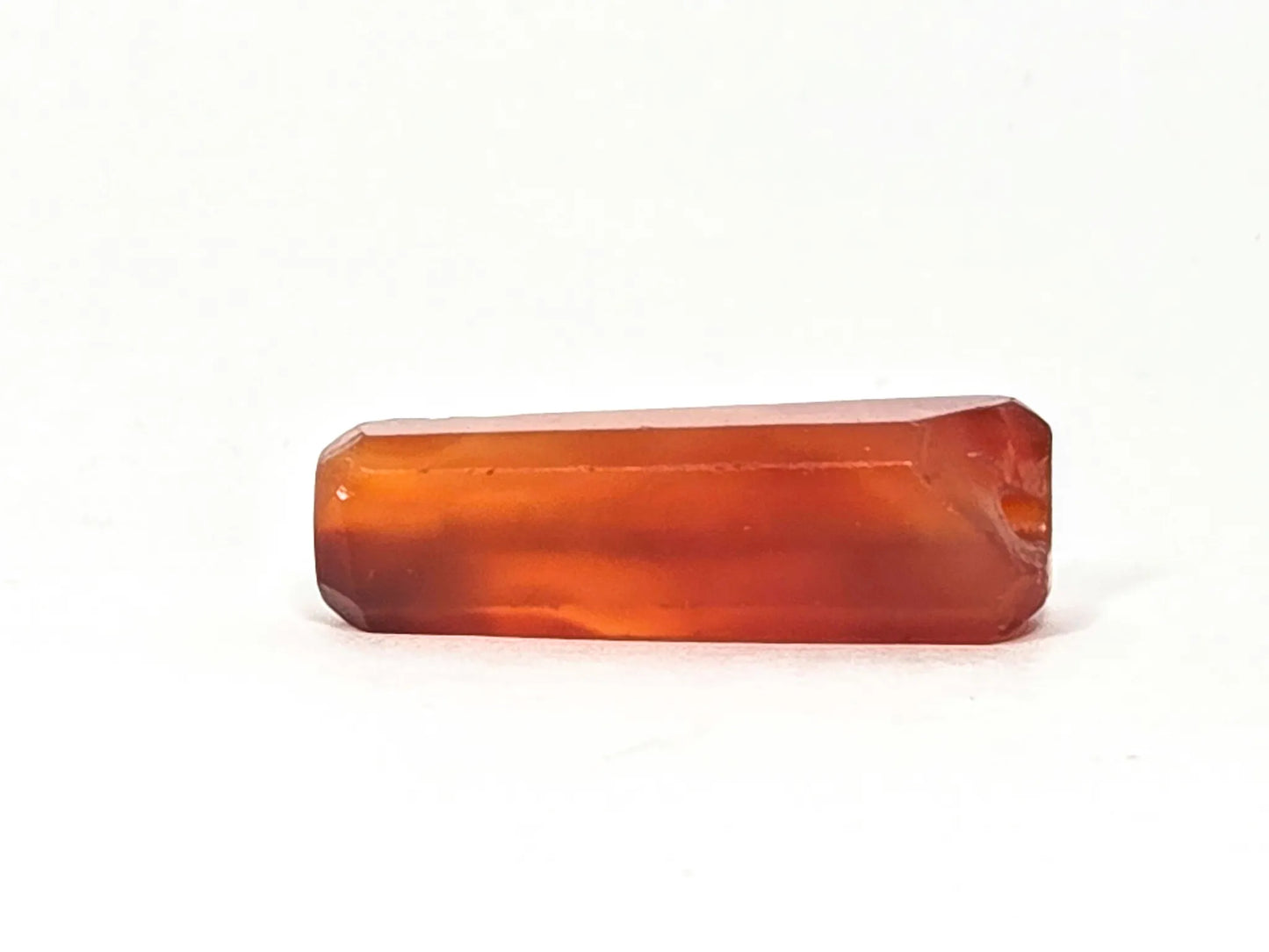 Top face of ancient beveled carnelian bead — flat rectangular surface with beveled edges, warm amber-orange translucent natural carnelian, chipping at right end visible