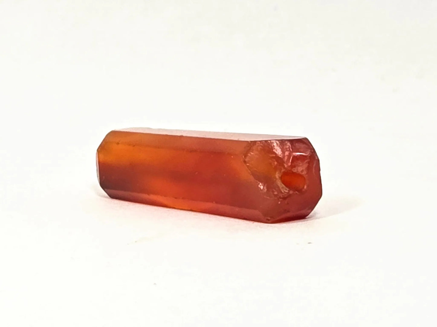 Second end of ancient beveled rectangular carnelian bead — worn oval drill hole and ancient chipping at end face, translucent carnelian body, unretouched
