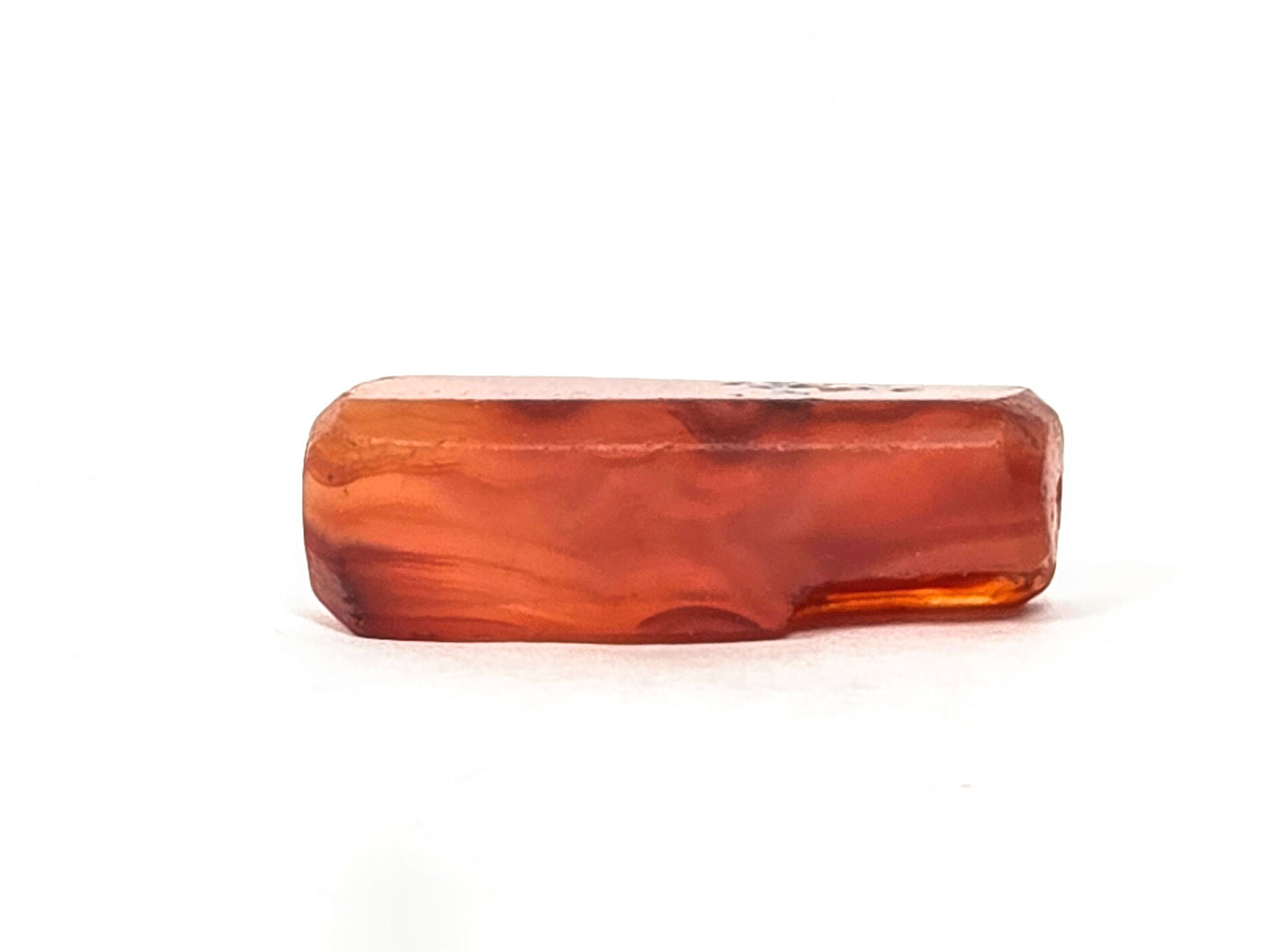 Anc-0626-CBev2, top flat face of beveled rectangular carnelian bead, ancient chipping at right end visible, unretouched
