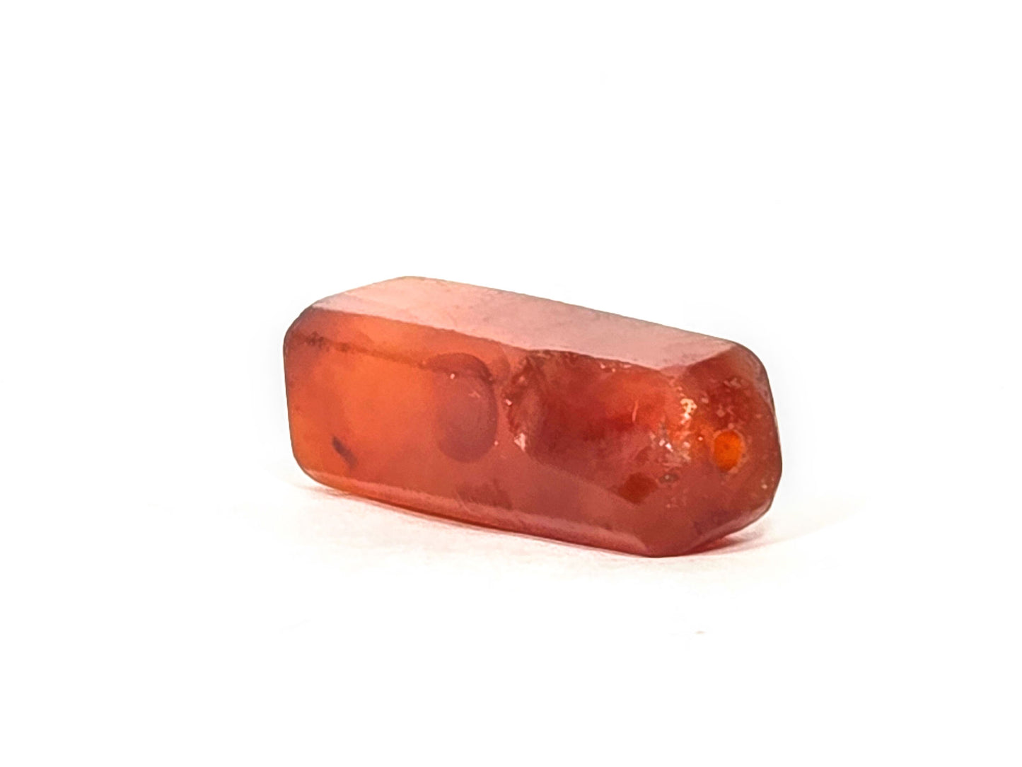 Anc-0626-CBev2, angled End A showing intact drill hole and significant ancient chipping, vivid orange-red carnelian, unretouched