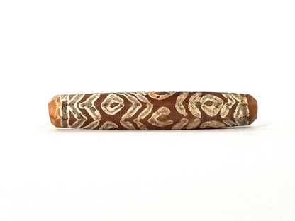 Ancient etched carnelian bead AC-101426-12E, first lateral profile showing dense cream-white twelve-eye and tiger wave motif — diamond-framed eye units alternating with chevron zigzag band lines across warm reddish-orange carnelian ground, eight-sided faceted cylinder form, 1500–2000 years old
