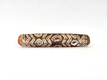 Third lateral profile of ancient etched carnelian bead AC-101426-12E showing octagonal faceted form clearly — flat facet planes and ridges between faces visible at edges, full-surface cream-white twelve-eye and tiger wave etching on warm reddish-orange carnelian, 1500–2000 years old