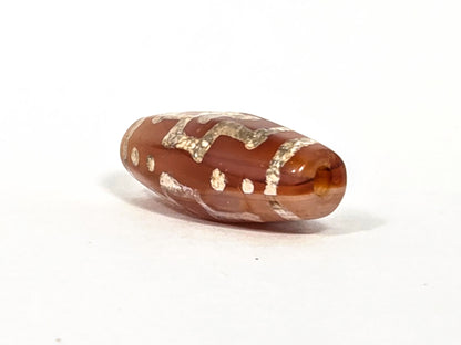Ac-080426-DCCS ancient carnelian dzi bead 29.1×12.2mm, angled view showing beveled shoulder profile and warm translucent drill end, unretouched