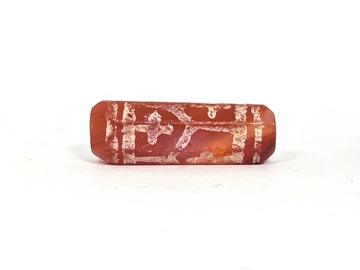 Ancient etched carnelian bead (AC-101026-CL6), first lateral profile showing cross and longevity motifs in heavily mineralised cream-white etching on deep red-orange translucent carnelian, tapered octagonal form, 500–1000 years old