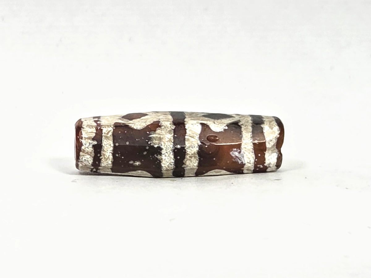 Second lateral profile of ancient etched carnelian bead showing reverse face with grid and band motif etching on warm amber-brown carnelian, octagonal faceted body with crystalline white etched surface, 31.1 mm × 10.4 mm