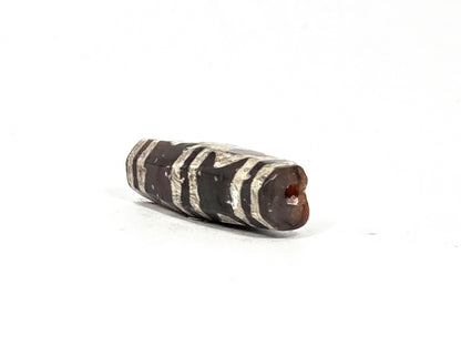 Angled end view of ancient etched carnelian bead AC-101226-EC showing drill hole aperture in warm reddish-orange carnelian tip, octagonal cross-section visible, silver-white etching bands along faceted barrel body