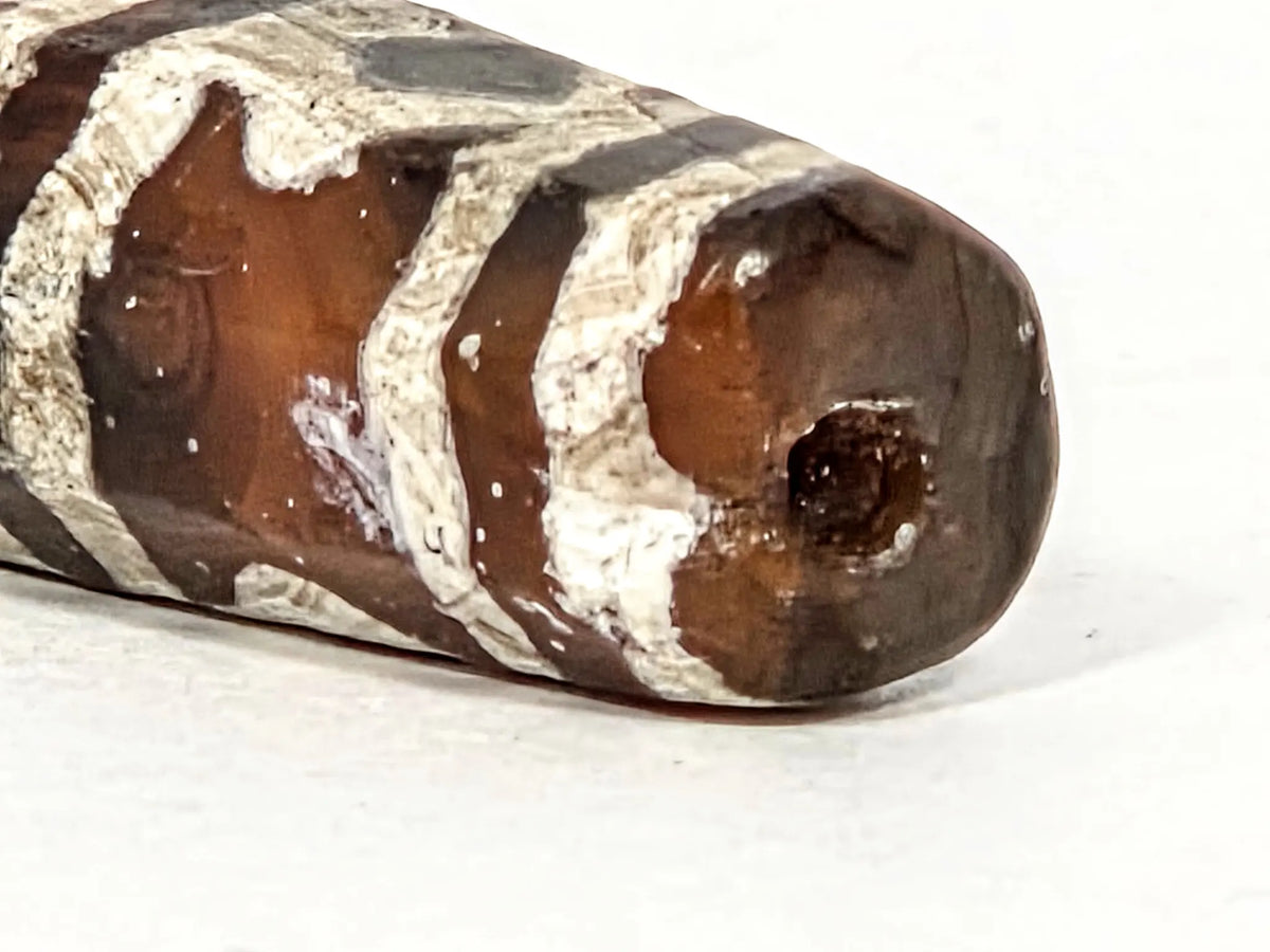 Macro close-up of ancient etched carnelian bead AC-101226-EC showing drill hole in warm amber-red carnelian tip, transition from etched motif bands to plain carnelian tip face, surface mineral texture detail