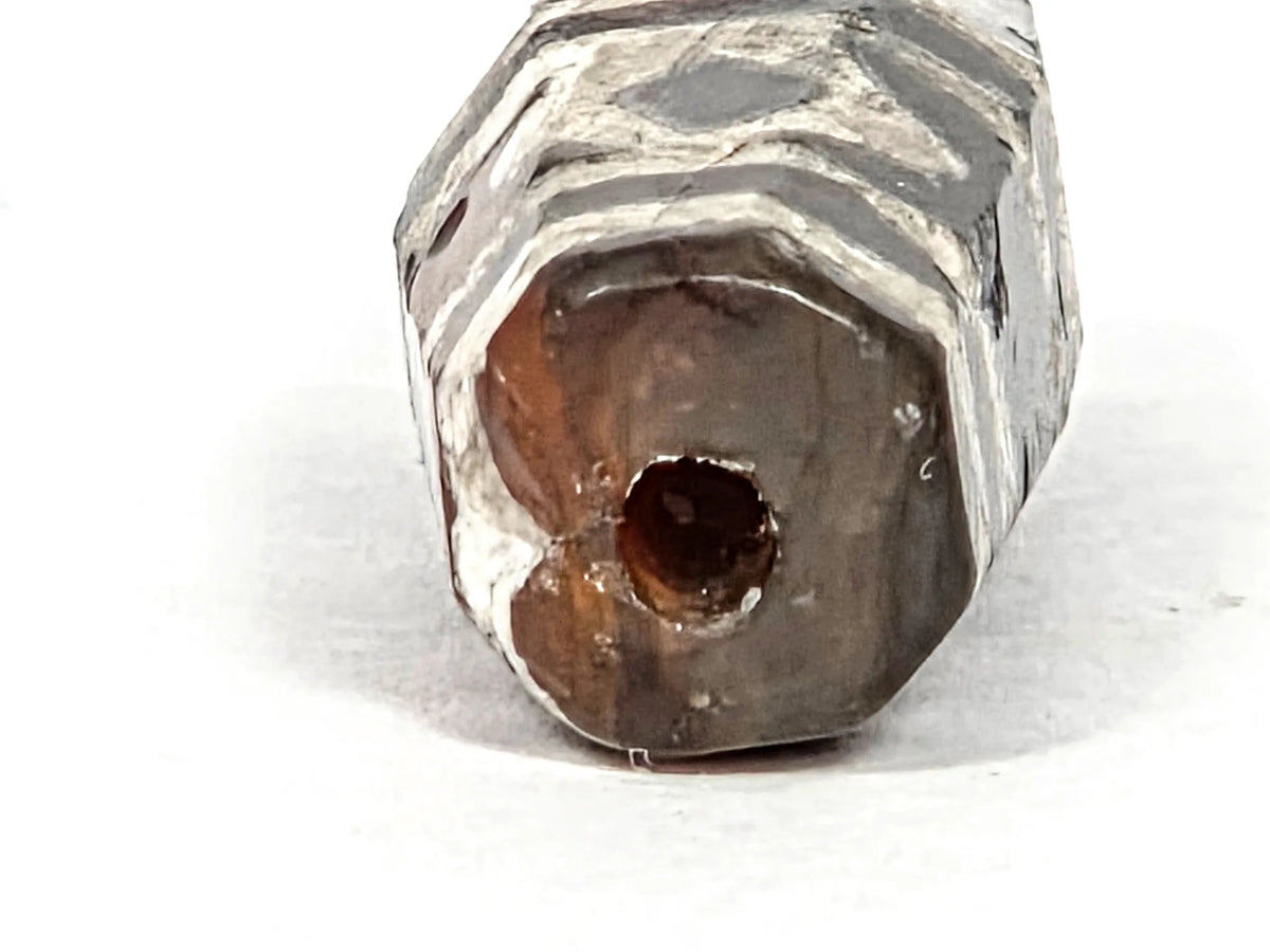 Macro detail of ancient etched carnelian bead showing octagonal faceted body with crystalline white lime etching, crafting-era indentation in carnelian surface covered by etching, confirming divot predates decoration, 700–1000 years old