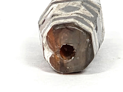 Macro detail of ancient etched carnelian bead showing octagonal faceted body with crystalline white lime etching, crafting-era indentation in carnelian surface covered by etching, confirming divot predates decoration, 700–1000 years old