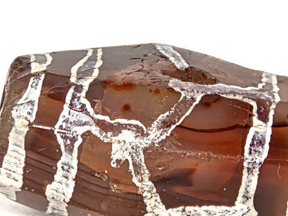 Extreme macro of medicine dig on ancient etched carnelian bead (AC-101026-CM2) showing deliberate excavation into carnelian surface with smooth worn edges, aged mineral deposits in interior, and surrounding white etching