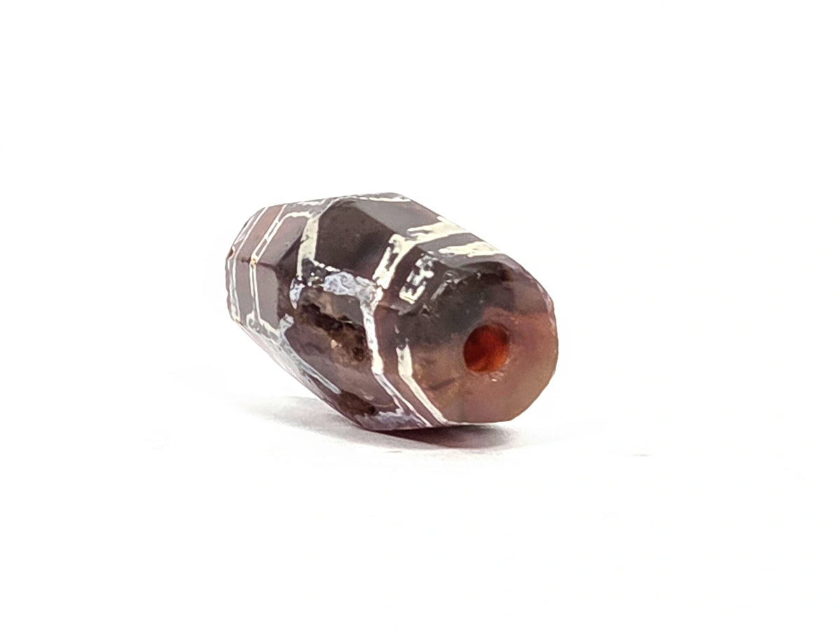 Angled end view of ancient carnelian tortoise shell longevity bead showing small drill hole, sharp octagonal facets, and deep reddish-orange carnelian interior visible at aperture