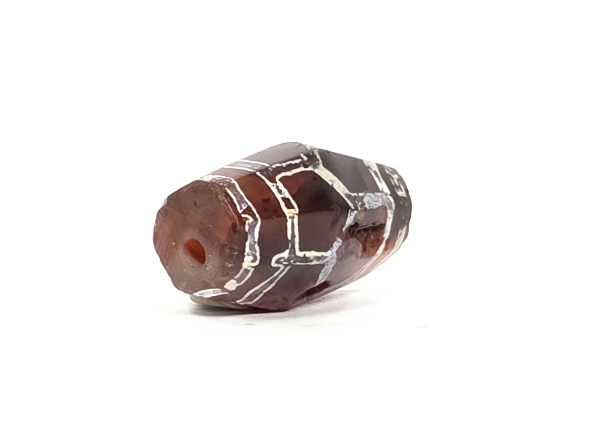 Opposite angled end view of ancient etched carnelian bead (AC-101026-CM2) showing second drill hole, octagonal form, and mineralised white etching continuing to the end faces