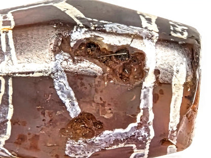 Extreme macro detail of ancient carnelian bead surface showing multi-layered crystalline white alkaline etching deposit, micro-pitted carnelian surface texture, and bloodspot deposits — evidence of 1000–1500 years of age