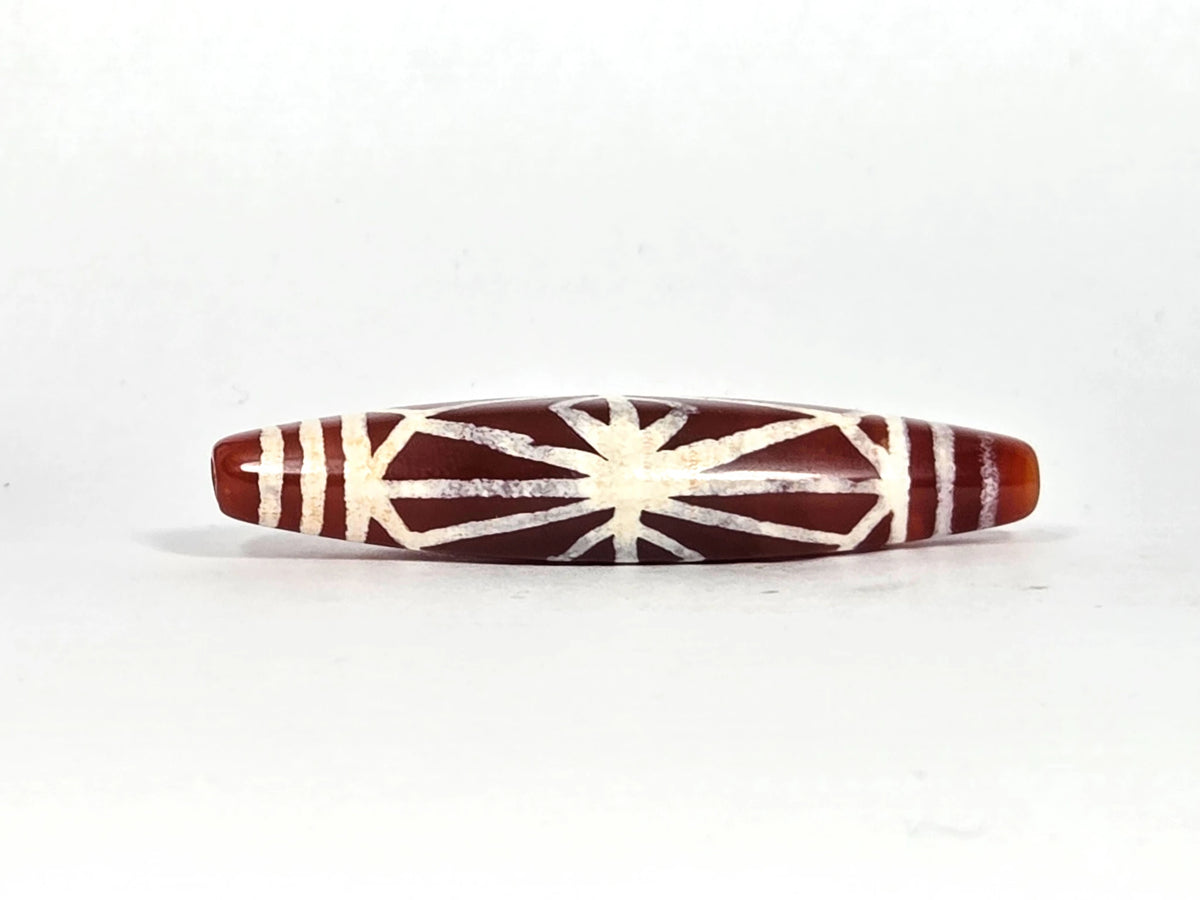 Third lateral profile of ancient etched carnelian starburst bead AC-101026-CS showing full spindle form, warm amber end caps, and complete cream-white starburst composition against deep sienna ground