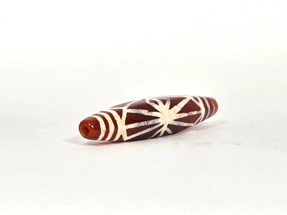 Angled end view of ancient carnelian starburst bead showing drill hole aperture set in warm amber-orange carnelian tip, with band lines and radiating motif visible, 500–700 years old