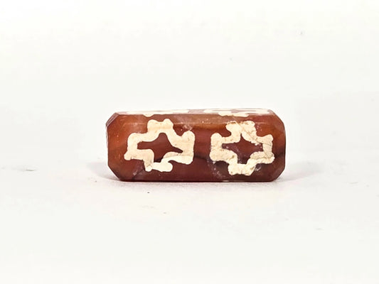 Ancient etched carnelian dzi bead (AC-100126-CM8), first face showing two floriate cross motifs with four-pointed star voids in heavily mineralized cream-white etching on warm red-orange carnelian, 500–1000 years old