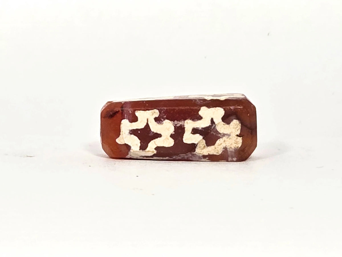 Second face of ancient carnelian eight-cross dzi bead showing two floriate cross motifs, thick cream-white alkaline etching on deep reddish-brown carnelian ground, 22.9 mm