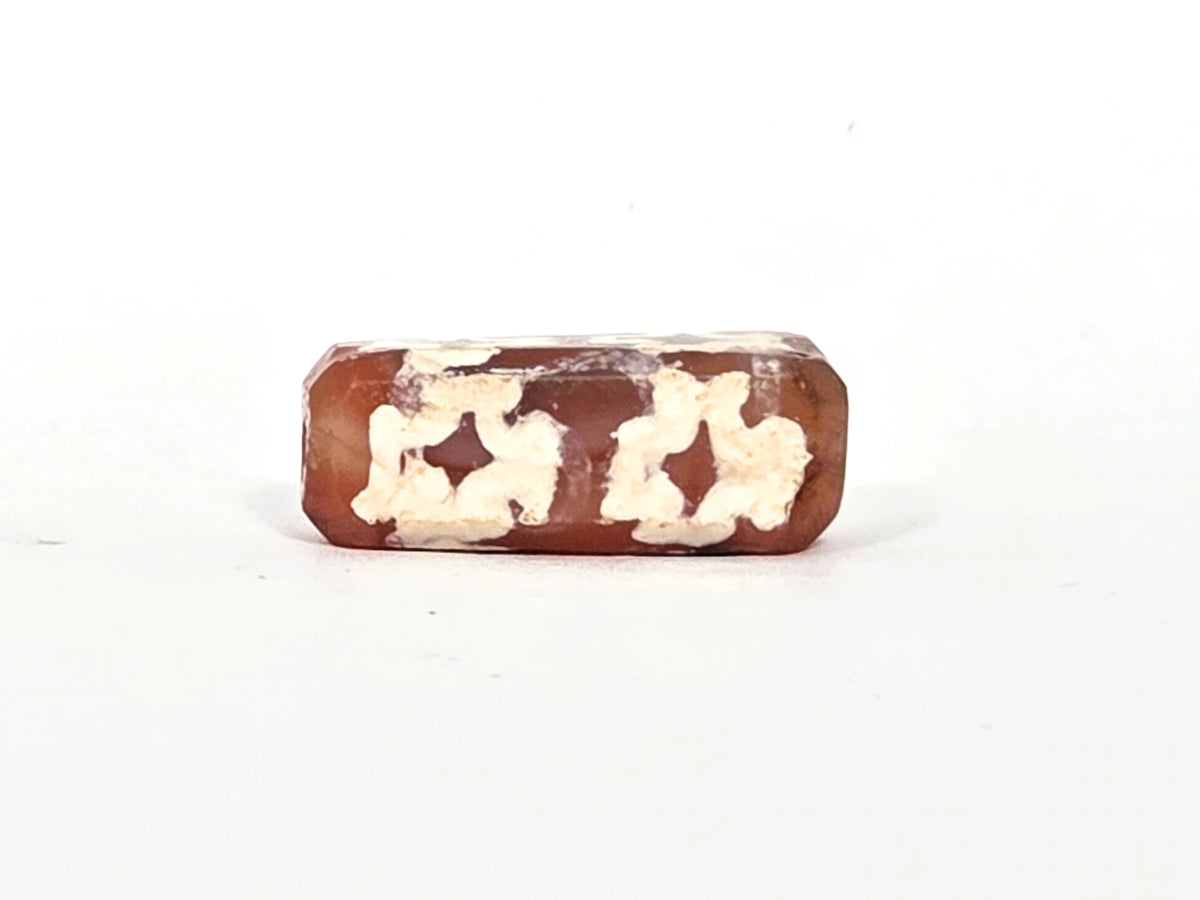 Third face of ancient etched carnelian dzi bead (AC-100126-CM8) showing two cross motifs with heavily weathered cream-white etching and warm red-orange translucent carnelian ground
